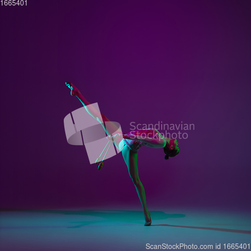 Image of Young female athlete, rhythmic gymnastics artist on purple background with neon light. Beautiful girl practicing with equipment. Grace in performance.