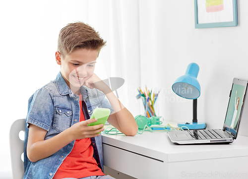 Image of happy boy with smartphone and laptop at home