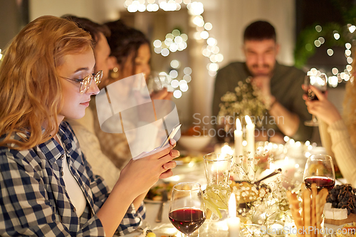 Image of woman with smartphone at dinner party with friends