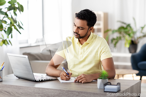 Image of indian man with notebook and laptop at home office