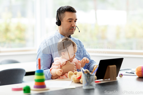 Image of father in headset working at home office with baby