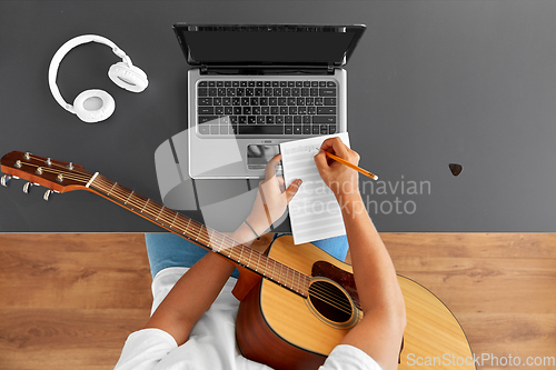 Image of man with guitar writing to music book at table