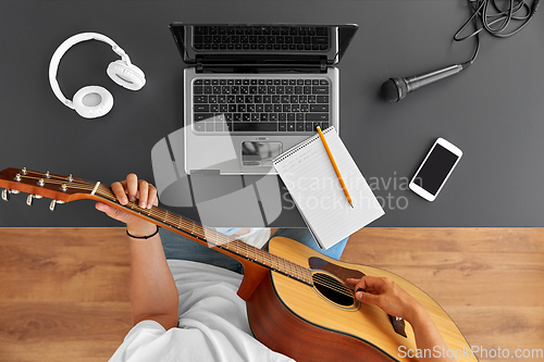 Image of young man with laptop playing guitar at table