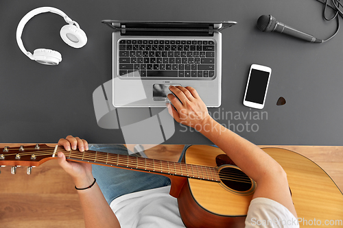Image of young man with laptop playing guitar at table