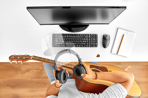 Image of young man with headphones and guitar at table