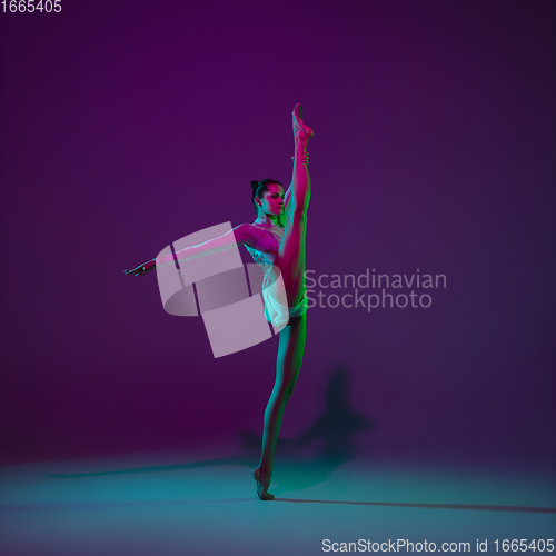 Image of Young female athlete, rhythmic gymnastics artist on purple background with neon light. Beautiful girl practicing with equipment. Grace in performance.