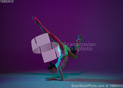 Image of Young female athlete, rhythmic gymnastics artist on purple background with neon light. Beautiful girl practicing with equipment. Grace in performance.