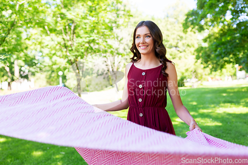 Image of happy woman spreading picnic blanket at park