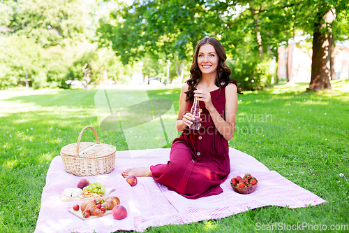 Image of happy woman with picnic basket and drink at park