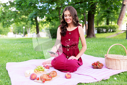 Image of happy woman with smartphone on picnic at park