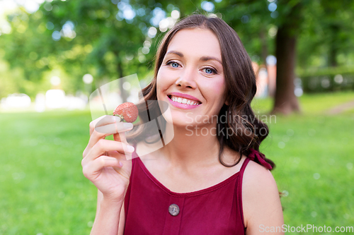 Image of happy woman eating strawberry at summer park