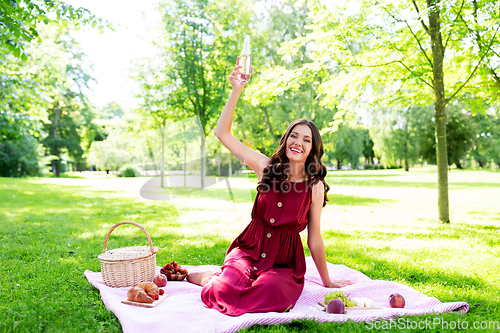 Image of happy woman with picnic basket and drink at park