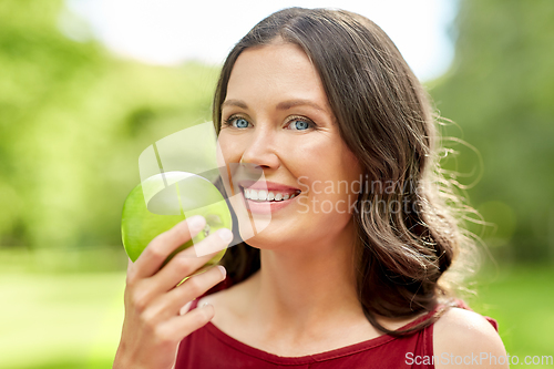 Image of happy woman eating green apple at summer park