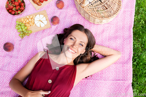 Image of happy woman lying on picnic blanket at summer park