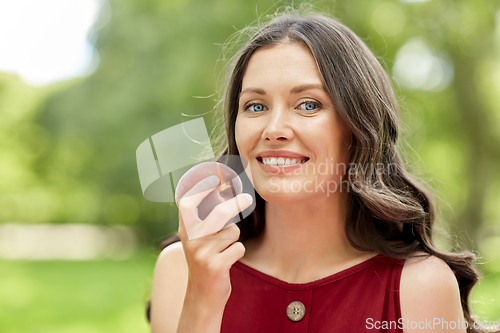 Image of happy woman eating peach at summer park