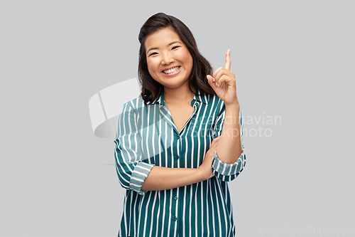 Image of happy asian woman pointing finger up on grey