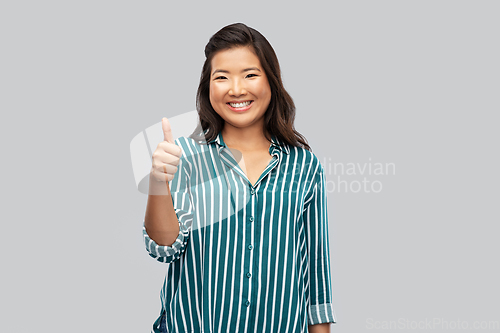 Image of happy asian woman showing thumbs up over grey