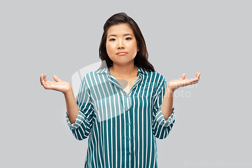 Image of sad asian woman shrugging over grey background