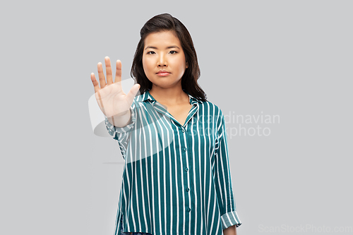 Image of asian young woman showing stop gesture over grey