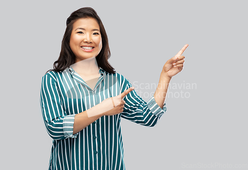 Image of happy asian woman pointing fingers up on grey