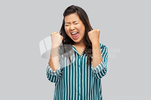 Image of happy asian woman celebrating success over grey