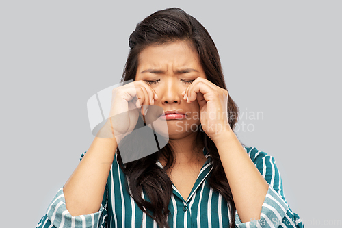 Image of sad asian woman crying over grey background