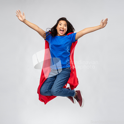 Image of happy asian woman in red superhero cape jumping