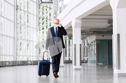 Image of old businessman in mask with travel bag at airport