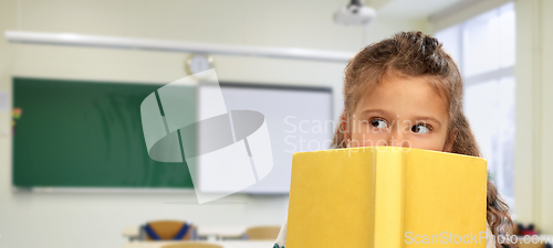 Image of little girl hiding behind yellow book at school