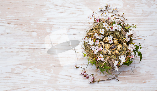 Image of Nest with Easter eggs and blooming branches on white wooden background