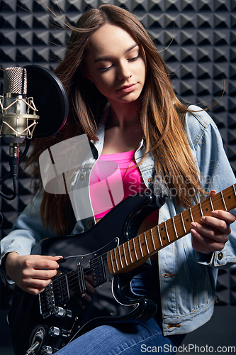 Image of Girl musician in recording studio playing electric guitar