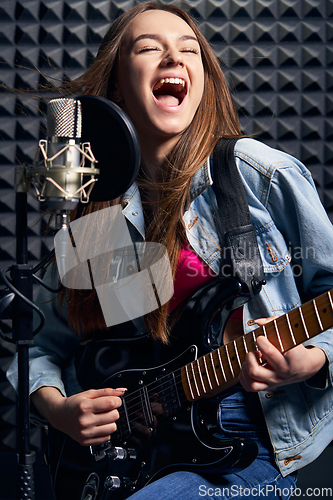 Image of Girl musician in recording studio playing electric guitar and singing in mic