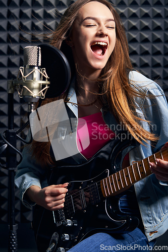Image of Girl musician in recording studio playing electric guitar and singing in mic