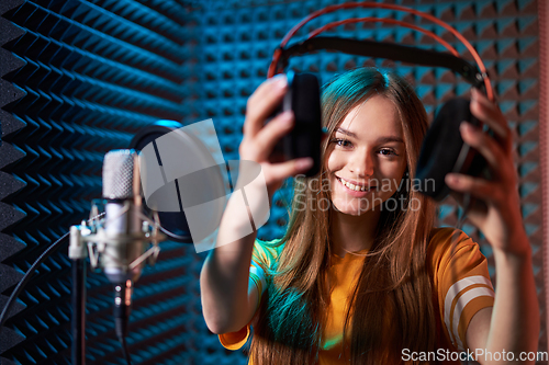 Image of Girl in recording studio in headphones with mic over absorber panel background with closed eyes