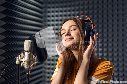 Image of Girl in recording studio in headphones with mic over absorber panel background with closed eyes