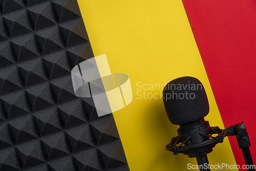 Image of Flat lay of microphone and acoustic foam panel, over red and yellow background