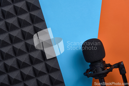 Image of Flat lay of microphone and acoustic foam panel, over blue and orange background