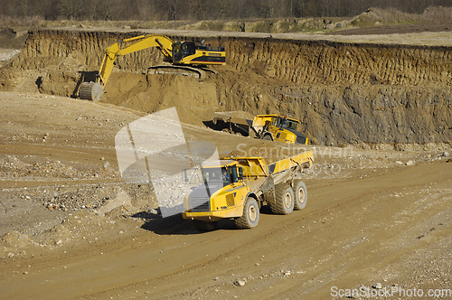 Image of Yellow dump trucks and excavator are working in gravel pit