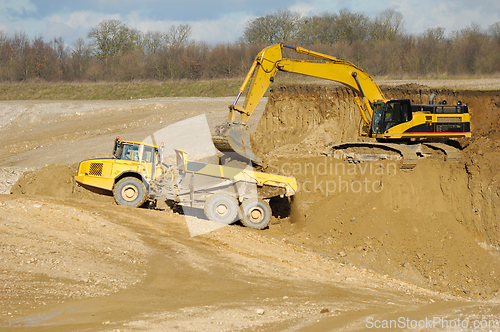 Image of Yellow dump trucks and excavator are working in gravel pit