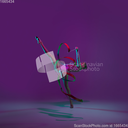 Image of Young female athlete, rhythmic gymnastics artist on purple background with neon light. Beautiful girl practicing with equipment. Grace in performance.