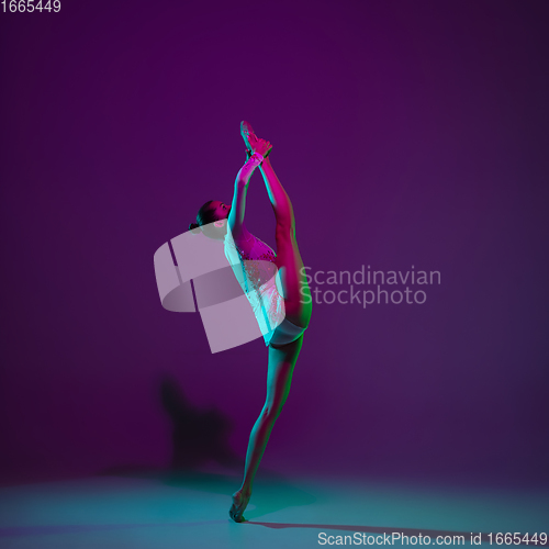 Image of Young female athlete, rhythmic gymnastics artist on purple background with neon light. Beautiful girl practicing with equipment. Grace in performance.