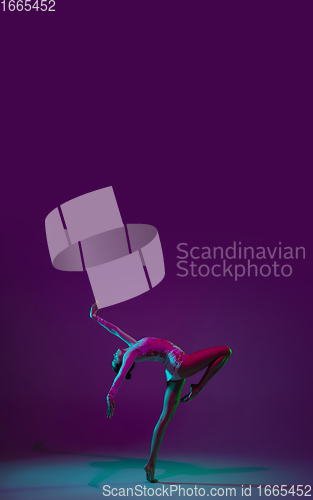 Image of Young female athlete, rhythmic gymnastics artist on purple background with neon light. Beautiful girl practicing with equipment. Grace in performance.