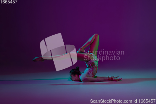 Image of Young female athlete, rhythmic gymnastics artist on purple background with neon light. Beautiful girl practicing with equipment. Grace in performance.