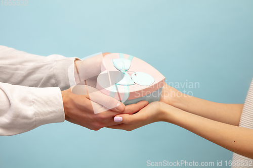 Image of Close up hands of beautiful couple in love holding giftbox on blue studio background. Valentine\'s Day, love and emotions concept