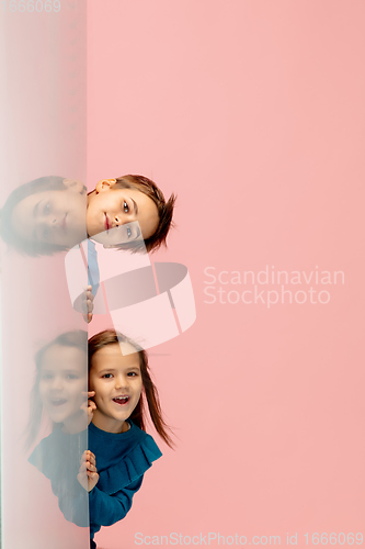 Image of Happy children isolated on coral pink studio background. Look happy, cheerful, sincere. Copyspace. Childhood, education, emotions concept