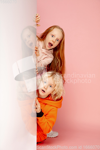 Image of Happy children isolated on coral pink studio background. Look happy, cheerful, sincere. Copyspace. Childhood, education, emotions concept