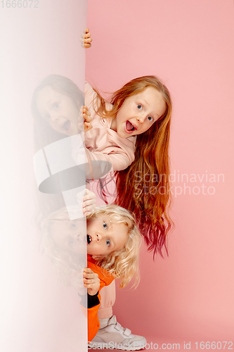 Image of Happy children isolated on coral pink studio background. Look happy, cheerful, sincere. Copyspace. Childhood, education, emotions concept