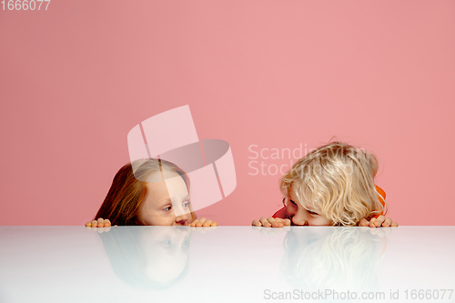 Image of Happy children isolated on coral pink studio background. Look happy, cheerful, sincere. Copyspace. Childhood, education, emotions concept