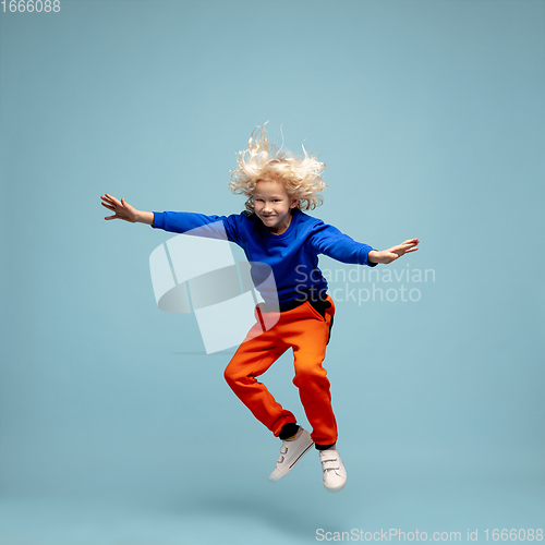 Image of Happy curly boy isolated on blue studio background. Looks happy, cheerful, sincere. Copyspace. Childhood, education, emotions concept