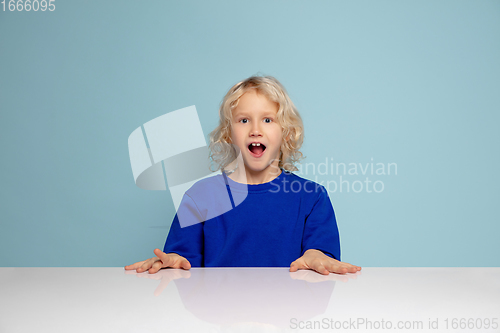 Image of Happy curly boy isolated on blue studio background. Looks happy, cheerful, sincere. Copyspace. Childhood, education, emotions concept